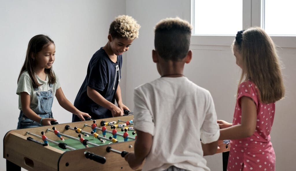 Group of multi-cultural cute children spending playtime with friends playing foosball together.